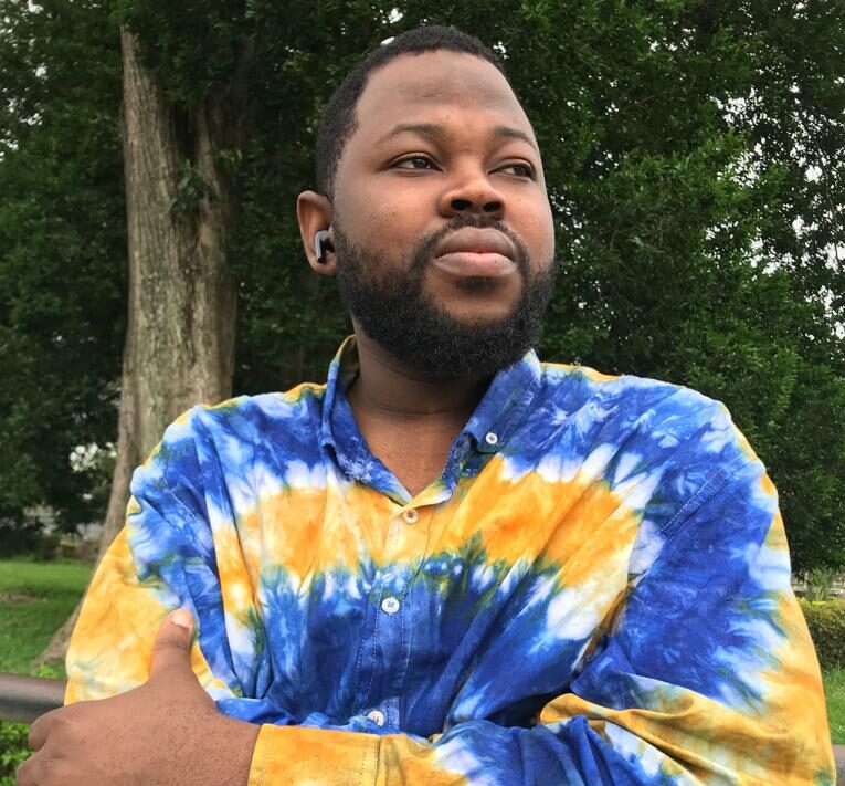 Photo of Author wearing a blue and yellow tie-dye shirt against some trees.