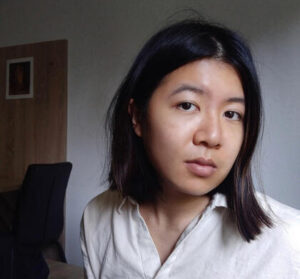 Author has short black straight hair and is wearing a white button down shirt against an office background.