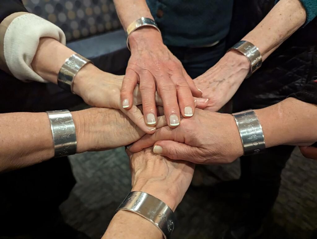 page six writing group hands in circle with silver bracelet