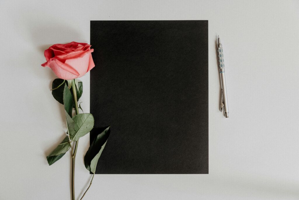 A black paper with a pen and a pink rose